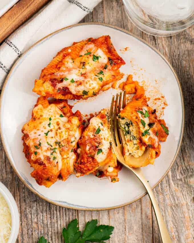 three stuffed shells on white plate with gold fork cutting into one of them