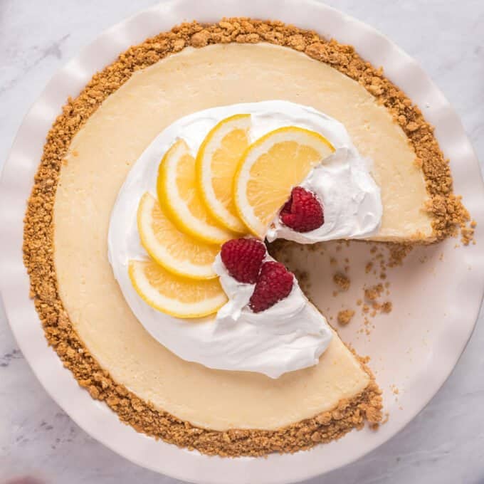 lemon pie with whipped cream lemons and raspberries on top with one slice taken out