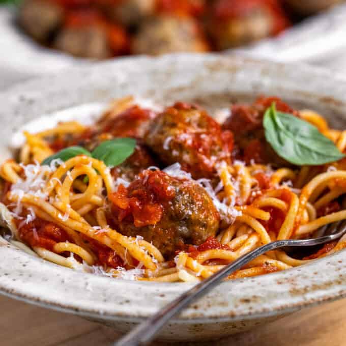 side view of a bowl of spaghetti and Italian meatballs with basil and parmesan cheese