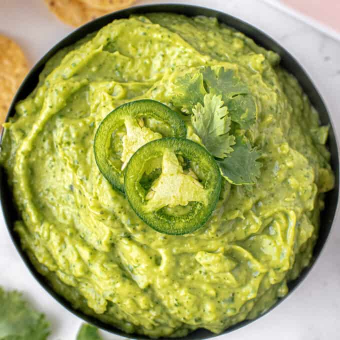 avocado dip in black bowl garnished with cilantro and jalapeno slices