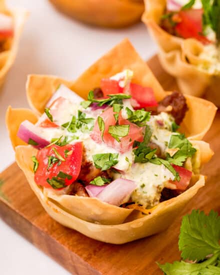 These crunchy Beef Taco Cups are a fun twist on taco night, or a delicious party appetizer! Baked instead of fried, they're packed with taco beef, refried beans, plenty of cheese, and all your favorite taco toppings!