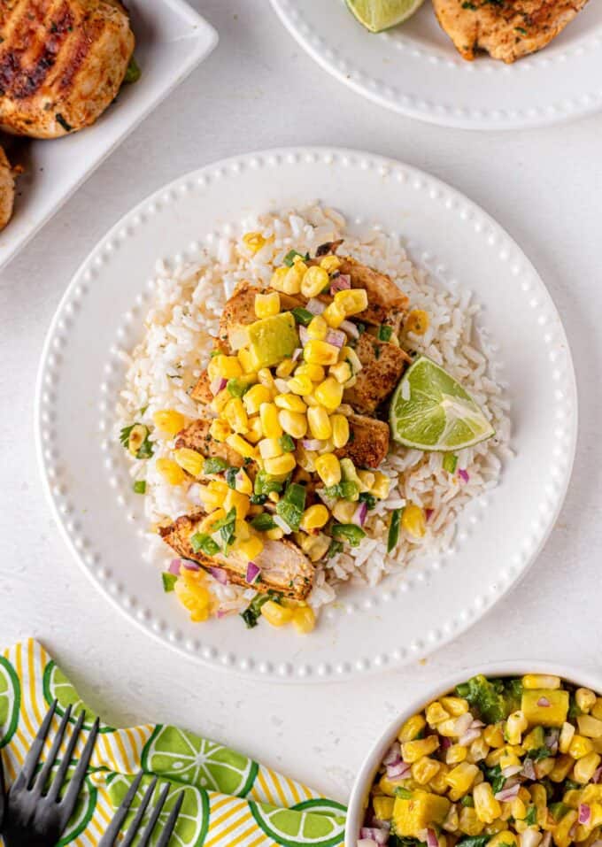 sliced grilled chicken on plate with rice topped with corn salsa and lime
