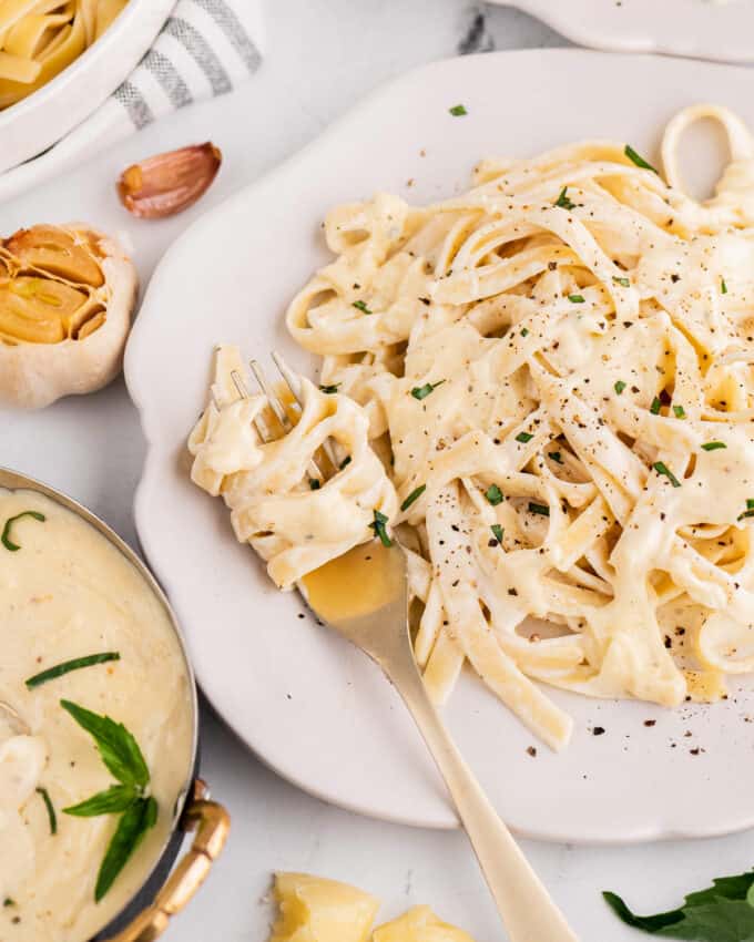 garlic fettuccine alfredo on white plate with gold fork
