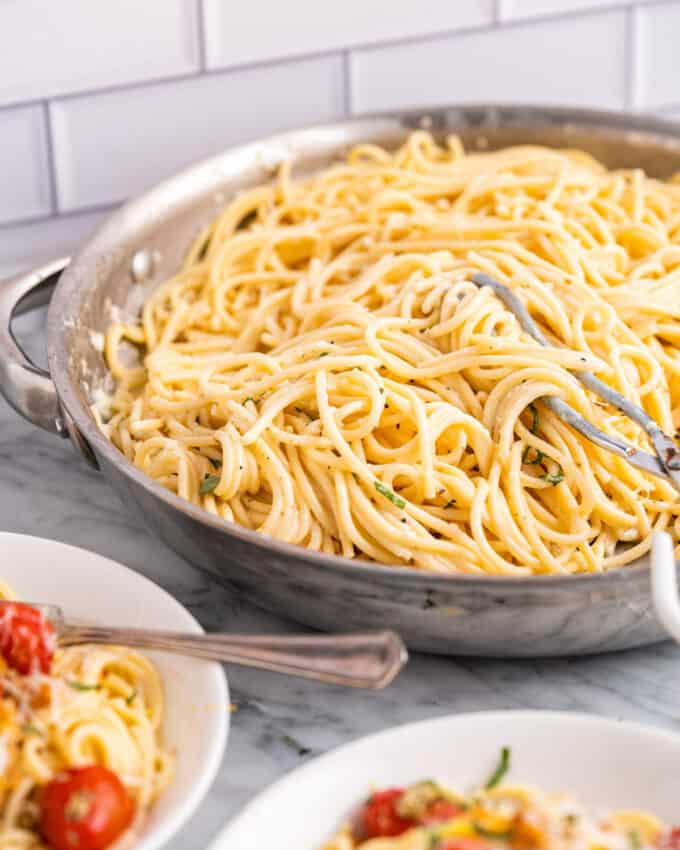 pan of creamy lemon pasta on counter with two bowls of pasta with chicken next to it