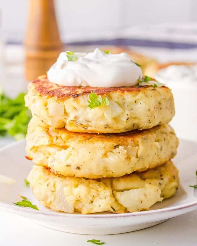 stack of 3 potato pancakes topped with sour cream on white plate