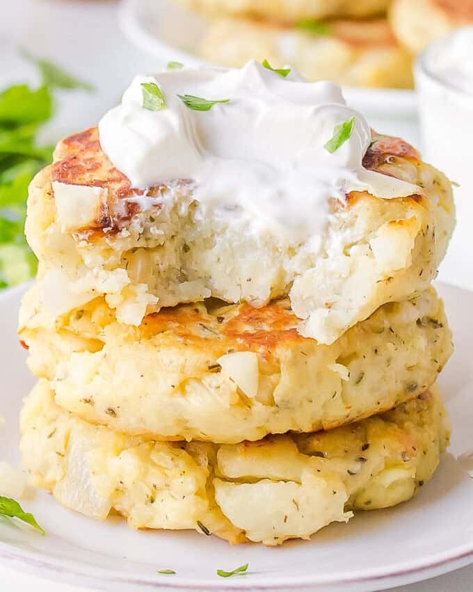 stack of potato cakes with a bite taken out of the top one with sour cream on top