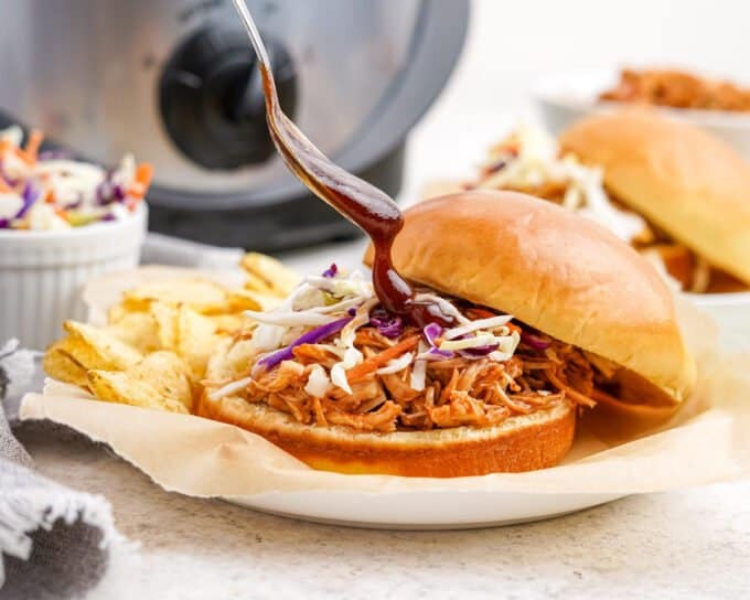 spooning bbq sauce onto pulled chicken sandwich