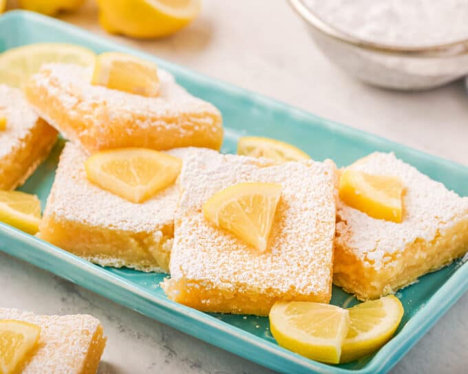 lemon bars on teal colored platter with lemon slices