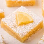 lemon bar cut in a square, dusted with powdered sugar, and with a lemon slice on top