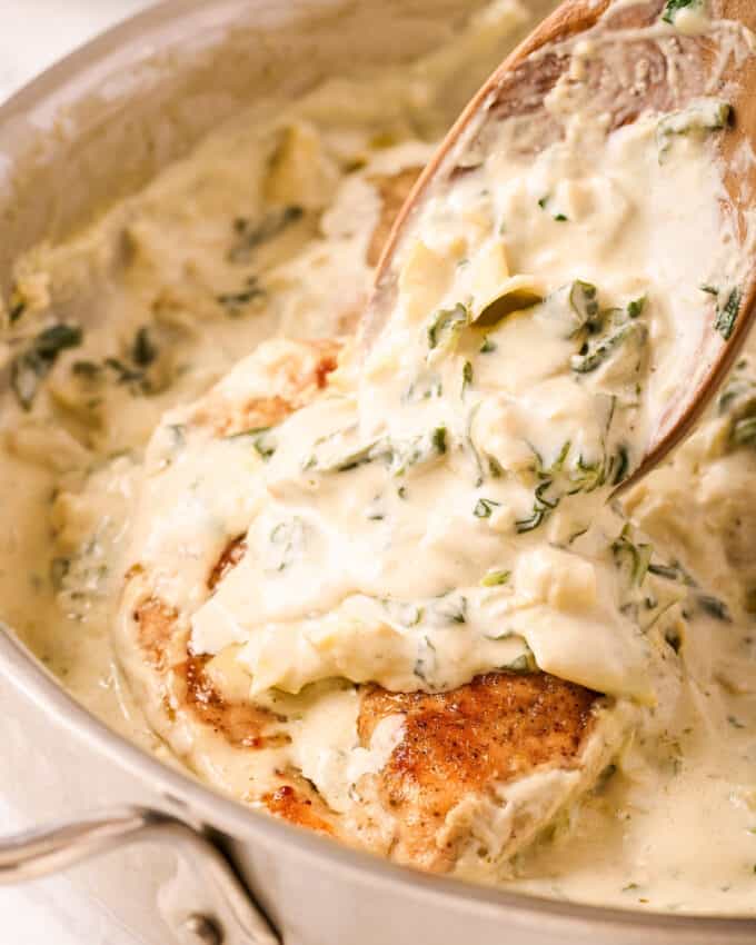 spooning spinach and artichoke sauce over a chicken breast in a skillet