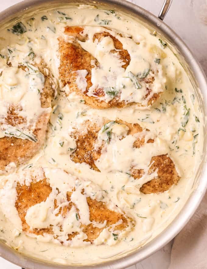 Everything you love about the classic spinach and artichoke dip, combined with an easy, one pan chicken dinner idea! Pan seared chicken breasts are smothered in an ultra creamy sauce loaded with chopped spinach and artichoke hearts!