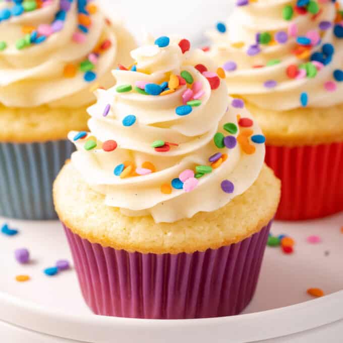 white plate of vanilla cupcakes with rainbow sprinkles