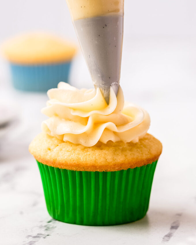 piping a swirl of buttercream frosting on cupcake with green liner