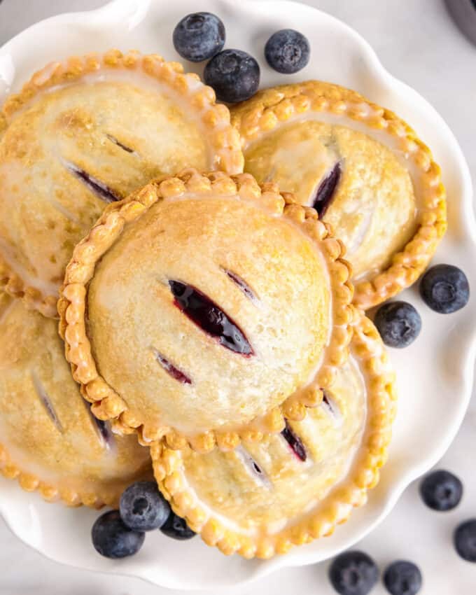 stack of blueberry cheesecake hand pies on white scalloped plate with fresh blueberries