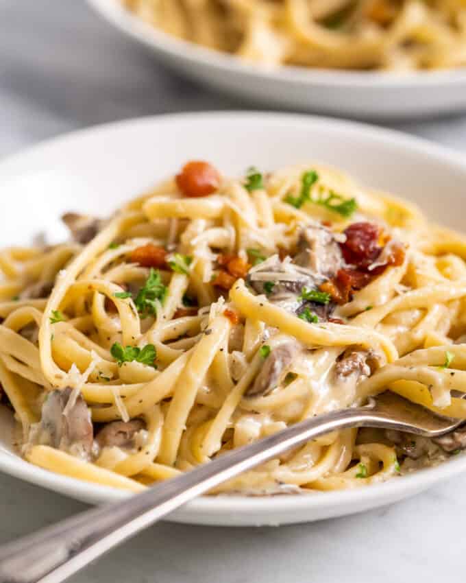 creamy pasta with mushrooms in a white bowl with a fork