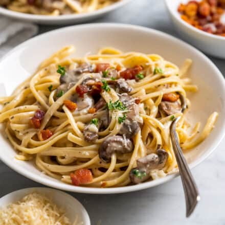 white shallow bowl of creamy mushroom pasta with fork in the bowl