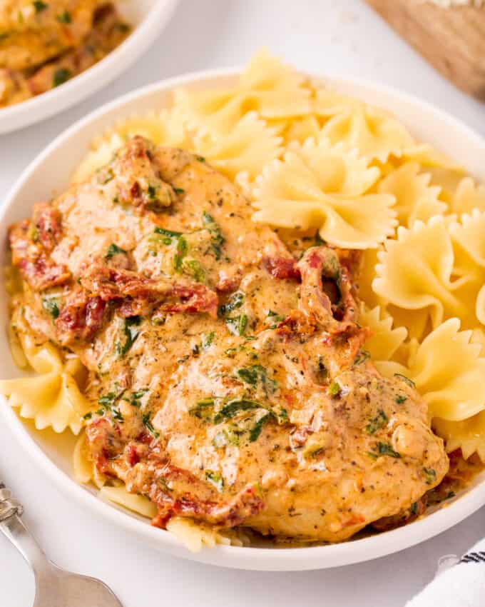 creamy tuscan chicken breast in white bowl with bowtie pasta