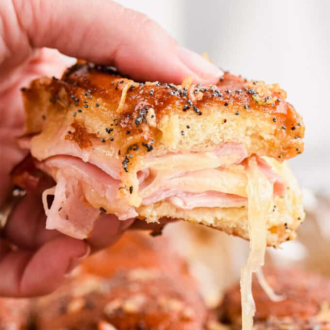 hand holding a ham and cheese slider with gooey cheese