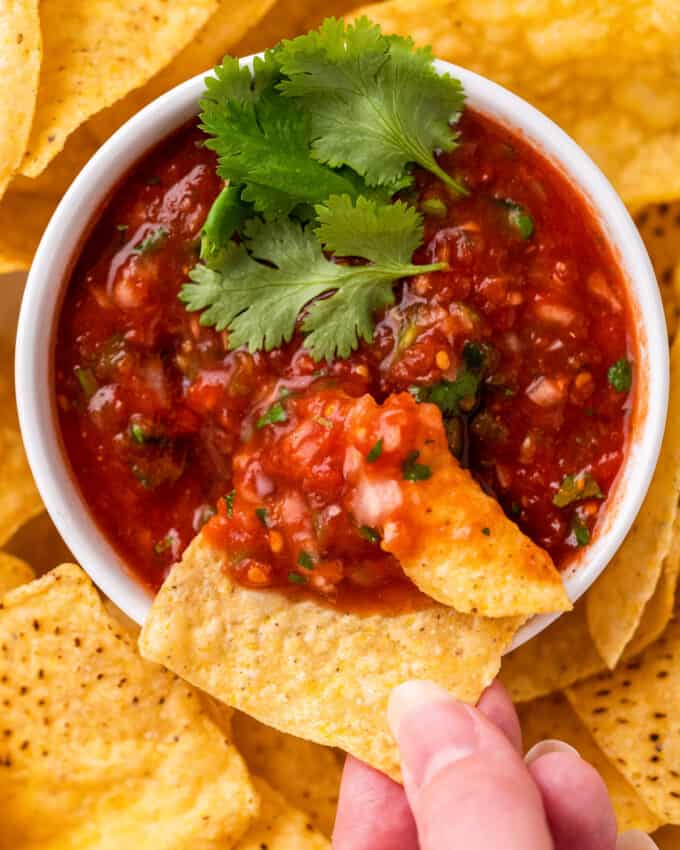 hand holding a tortilla chip with plenty of salsa on it