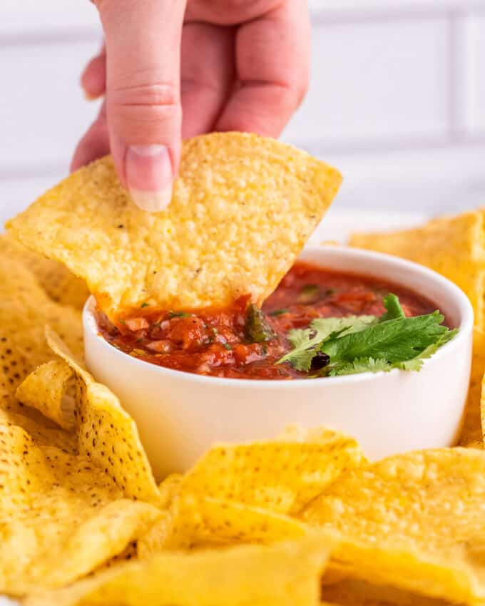 dipping a chip into a white bowl of salsa