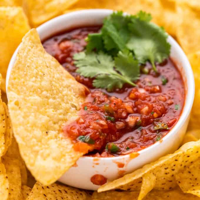 white bowl of salsa with tortilla chip dipped in it