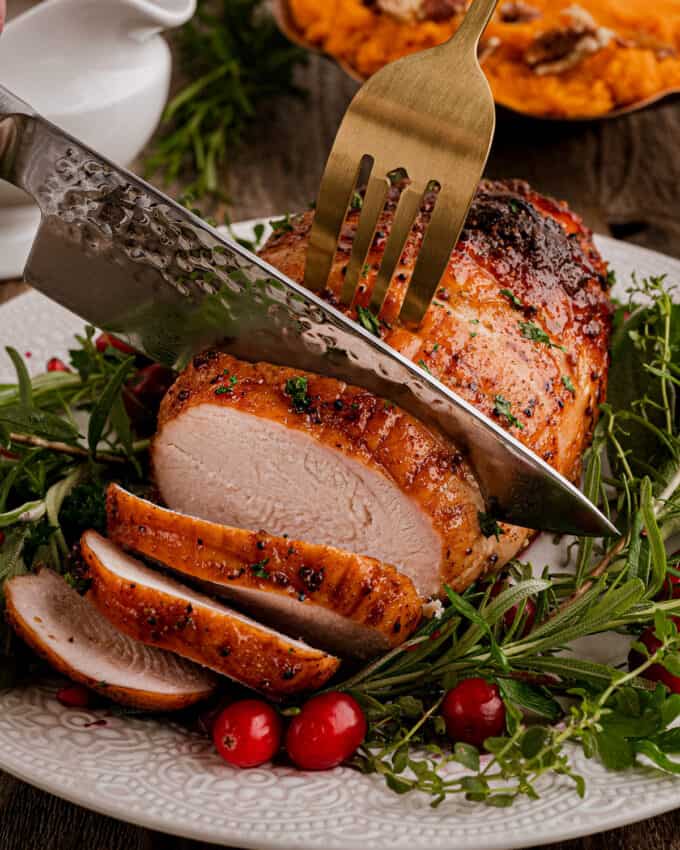 carving a boneless turkey breast with a knife and serving fork on a white platter