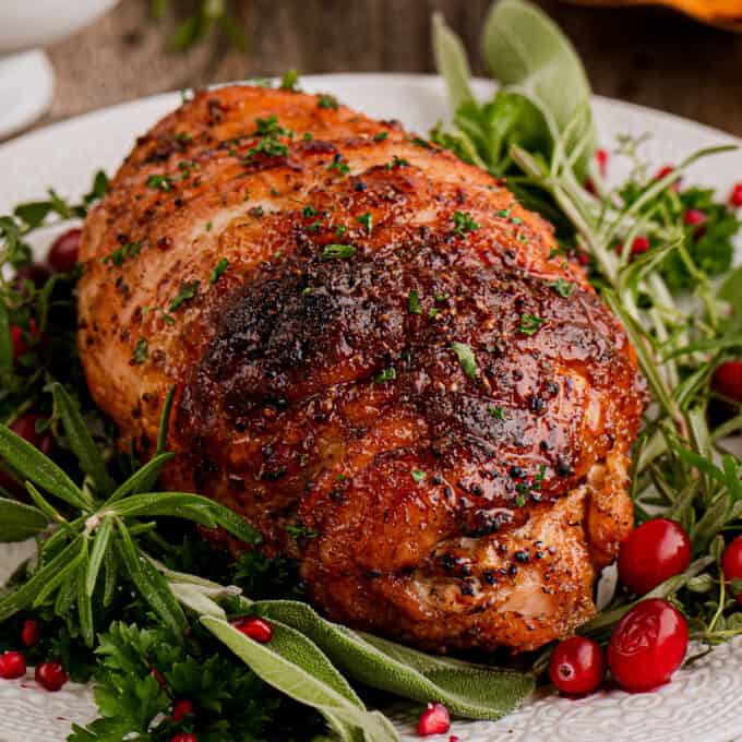 roasted boneless turkey breast on a white plate with herbs and cranberries