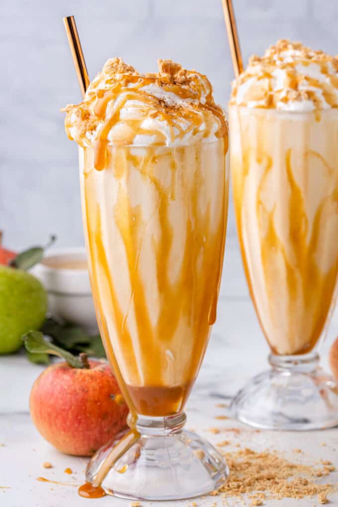 two milkshake glasses with an apple pie milkshake drizzled with caramel