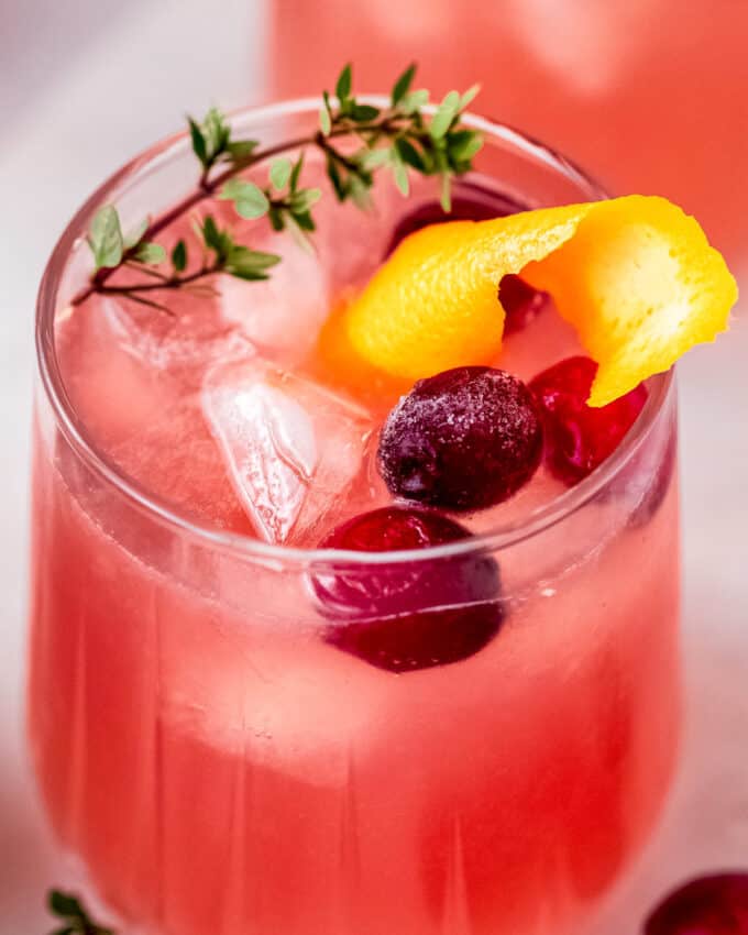 close up view of a glass full of cranberry orange cocktail with garnishes