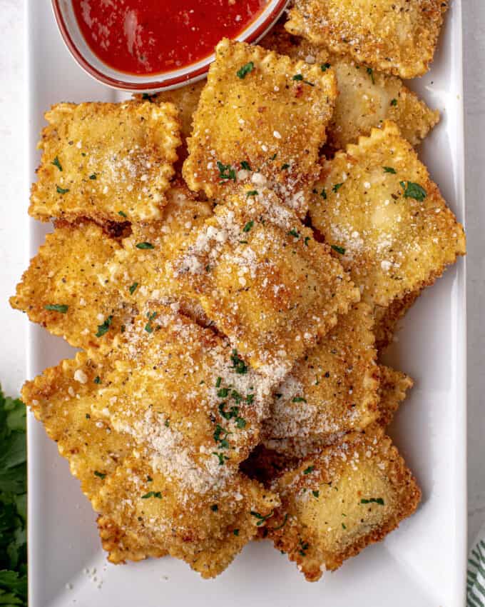 pile of toasted ravioli on white platter with a small bowl of marinara sauce