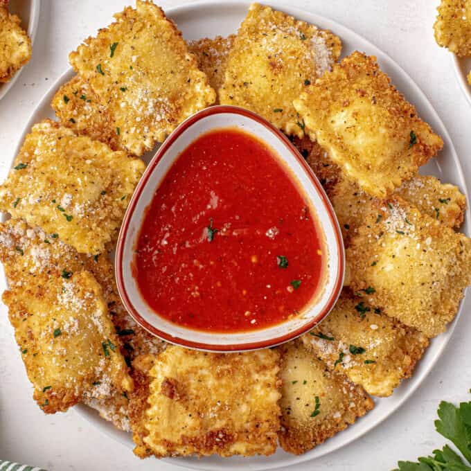 round white plate of fried ravioli with a bowl of marinara sauce in the center