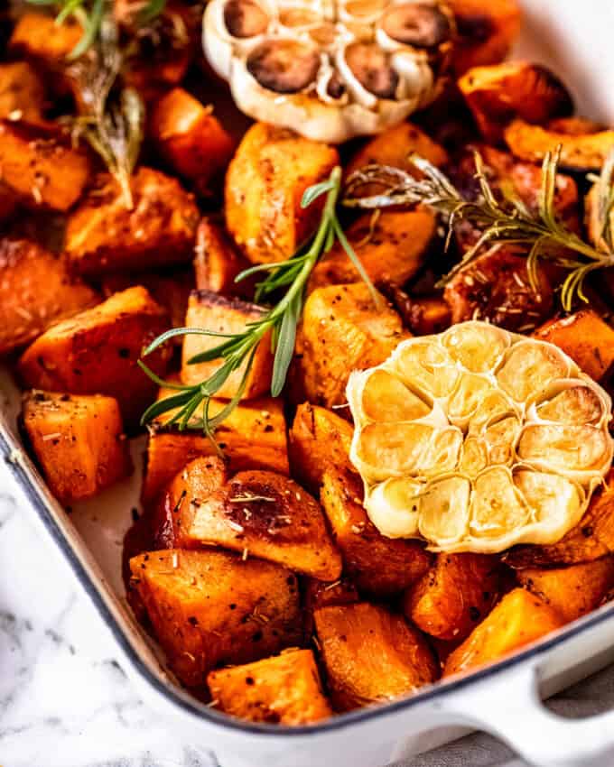 These Garlic Roasted Sweet Potatoes are a fantastic savory side dish for your family dinner or holiday meal. Diced sweet potatoes are seasoned and roasted with fresh herbs along with a head of garlic, which adds amazing flavor!