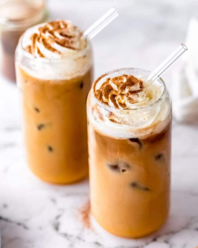iced pumpkin spice lattes in clear glasses with straws and whipped cream and cinnamon