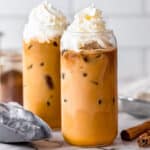 two clear glasses of iced pumpkin spice latte with whipped cream