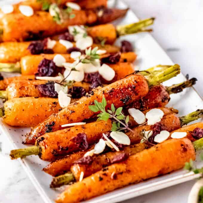 roasted carrots on white platter topped with almonds and cranberries