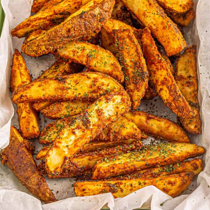 pile of crispy baked potato wedges on tray with parchment paper