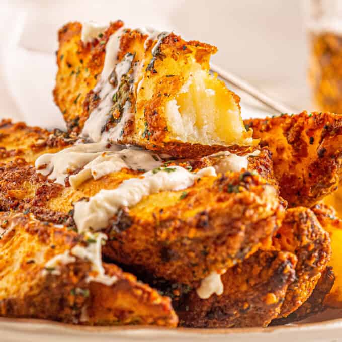 pile of baked potato wedges drizzled with ranch dressing