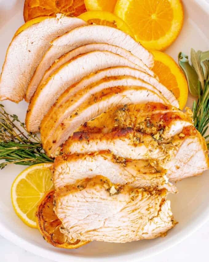 sliced roasted turkey breast on white platter with oranges and herbs
