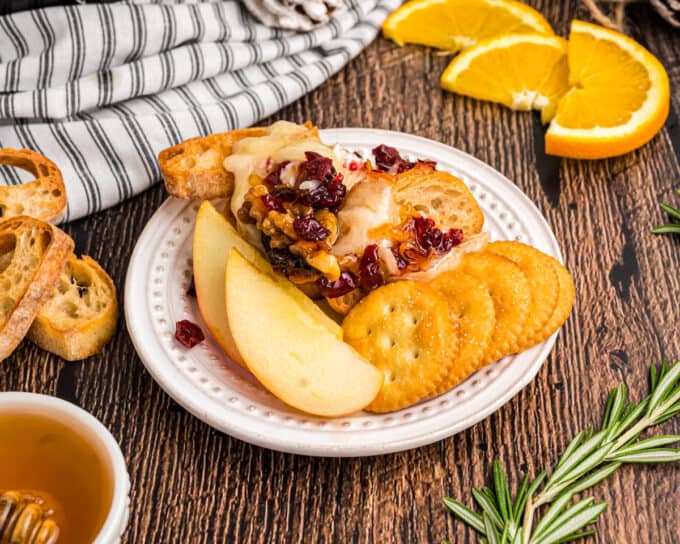 small white plate of baguette slices covered in gooey brie with cranberries, walnuts, and honey