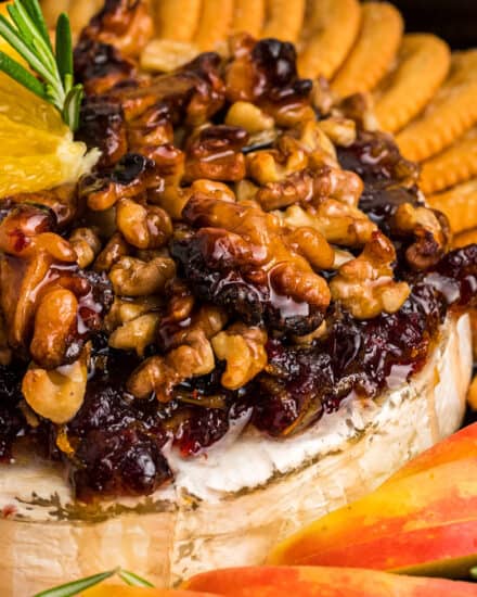 This baked brie recipe is perfect for the holidays, or any party! A wheel of brie is topped with an orange/cranberry spread, crunchy walnuts, and floral honey, then baked until perfectly gooey. Serve with baguette slices, apples, crackers, and more!