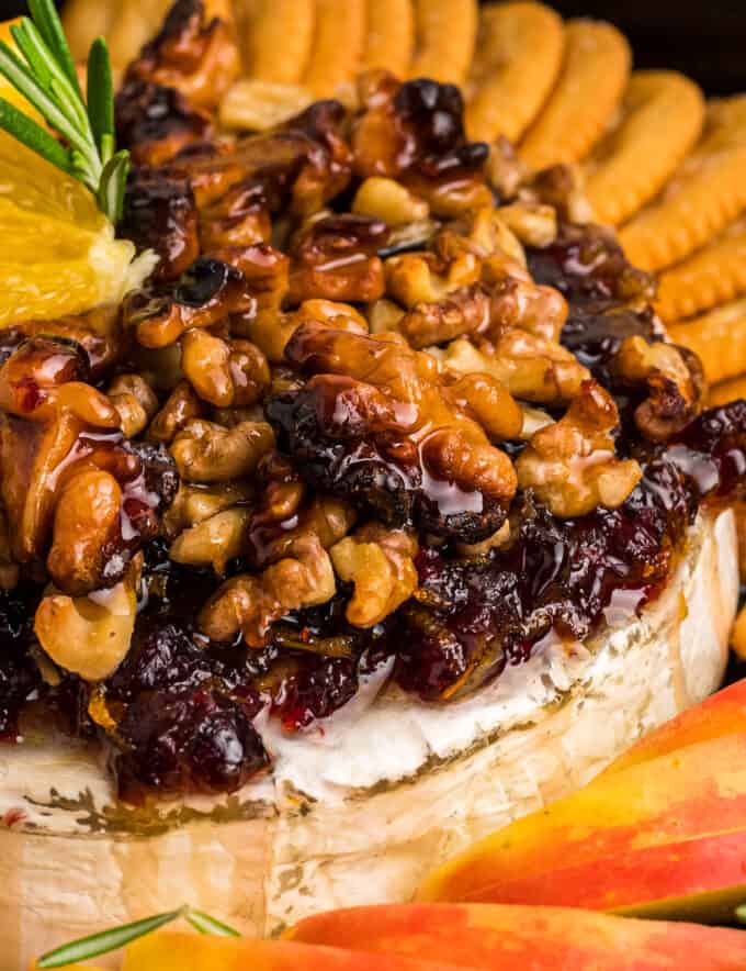 This baked brie recipe is perfect for the holidays, or any party! A wheel of brie is topped with an orange/cranberry spread, crunchy walnuts, and floral honey, then baked until perfectly gooey. Serve with baguette slices, apples, crackers, and more!