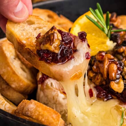 dipping a baguette slice into gooey baked brie topped with cranberries and walnuts