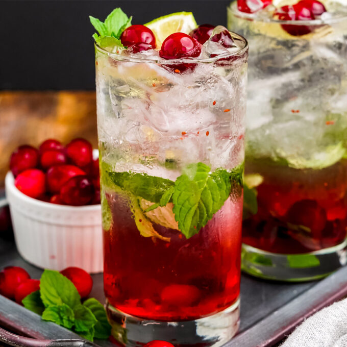 two tall glasses of cranberry mojito on metal tray with bowl of cranberries