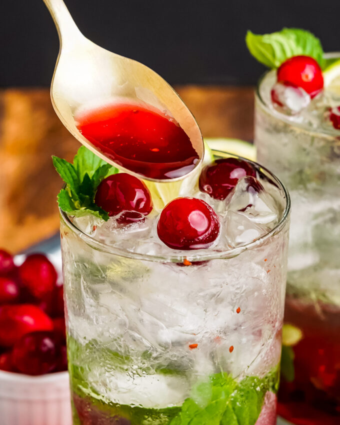 pouring cranberry syrup into a cranberry mojito cocktail