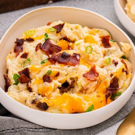 white bowl of mashed potato casserole topped with cheese, bacon, and green onions