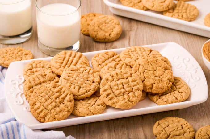 pile of peanut butter cookies on a white platter with glasses of milk near by