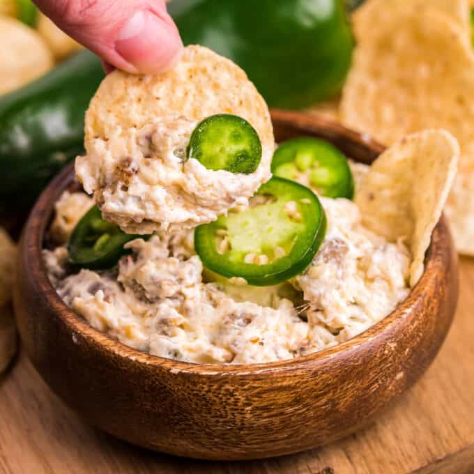 scooping some sausage dip with jalapenos onto a tortilla chip