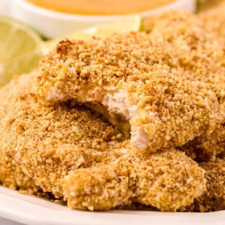 cashew crusted chicken tenders on plate, with a bite taken out of one of the chicken tenders