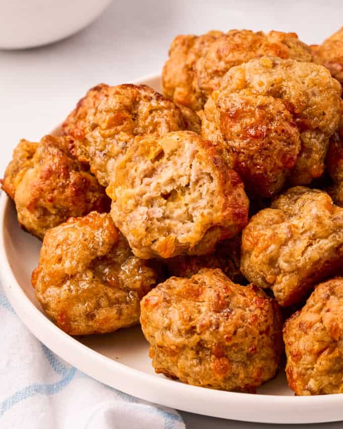 pile of sausage balls on white plate with one bitten in half