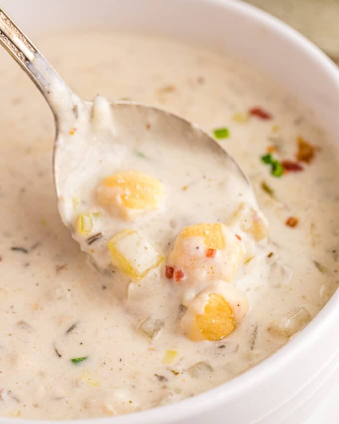 spoonful of clam chowder soup in a white bowl with oyster crackers on top